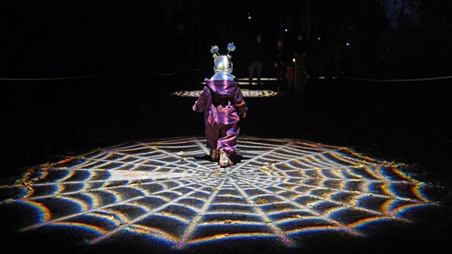 A child illuminated by a spider web shaped light at Wimpole Estate's Halloween at Wimpole trail
